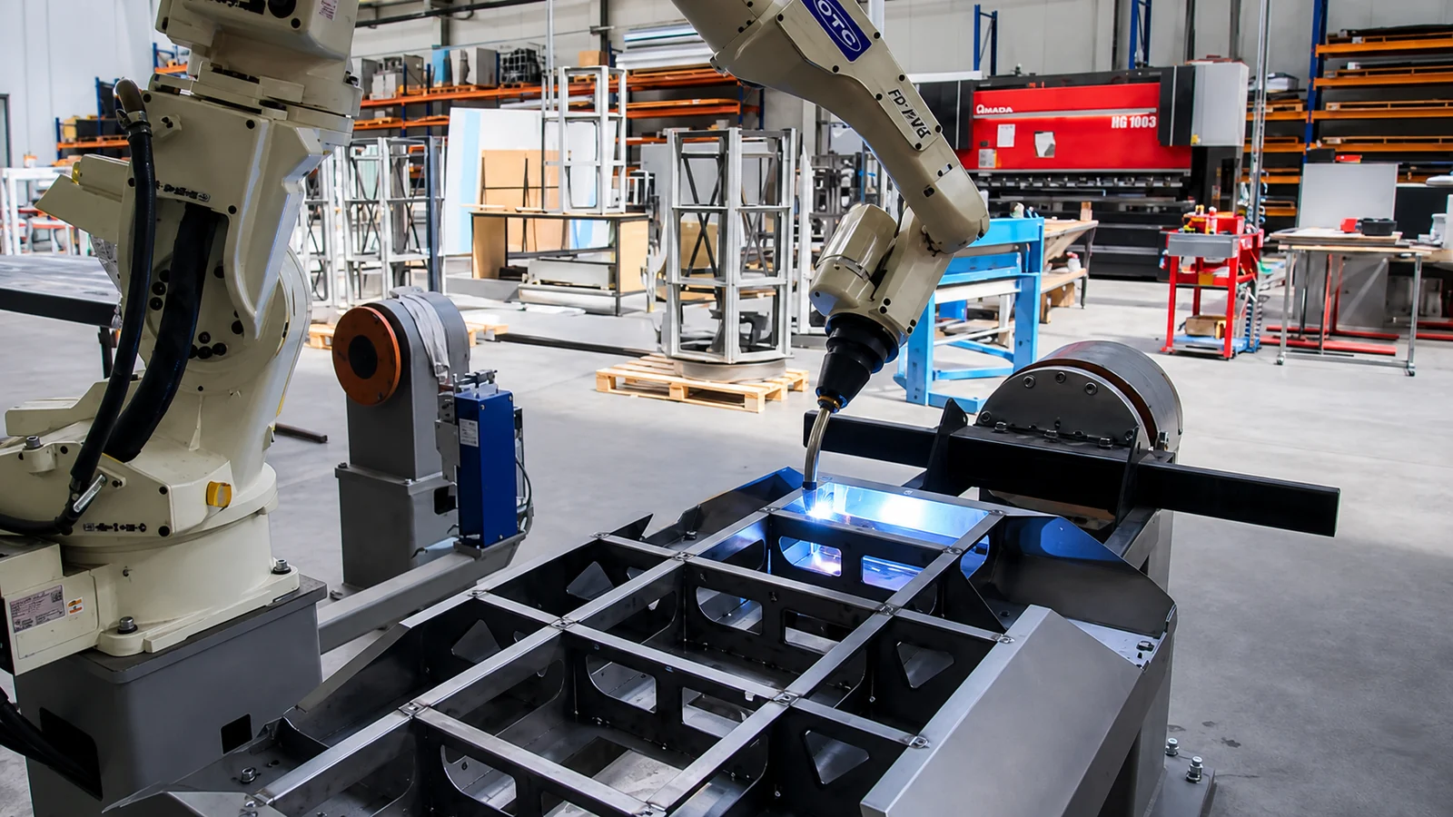 The OTC robotic cell — the arm welding a chassis on the positioner, the second positioner standing on the left