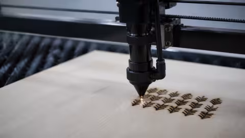 The CO2 laser head engraving a pattern into a light wood panel, over a honeycomb bed