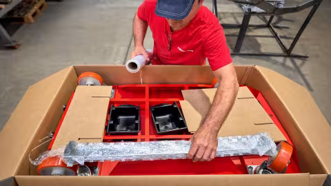 A worker packing a red NEON SMART trolley into a cardboard box with stretch film