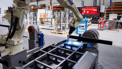 The OTC robotic cell — the arm welding a chassis on the positioner, the second positioner to the left